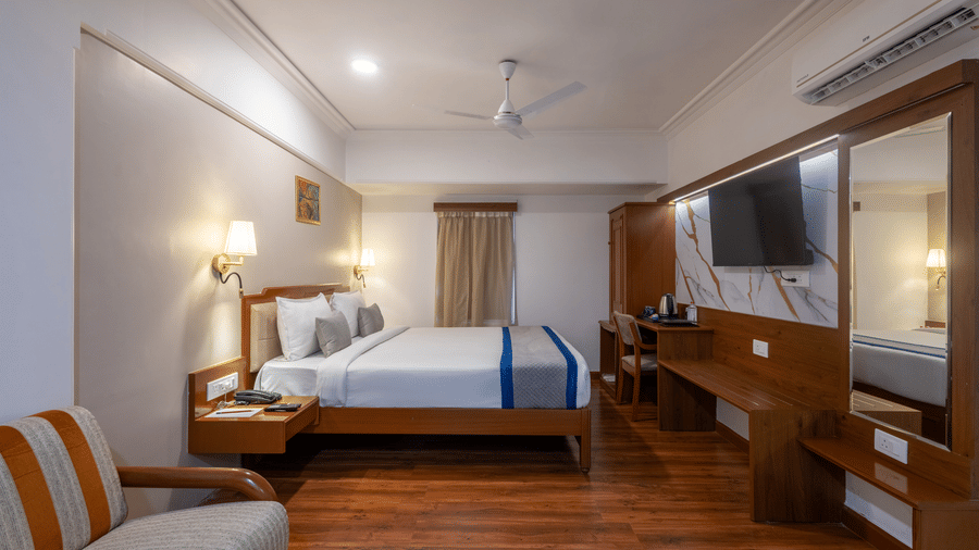 Wide view of a king-sized room showing the bed, built-in wooden furniture, and a full-length mirror behind the TV at Pravasa Stay, Vadodara.