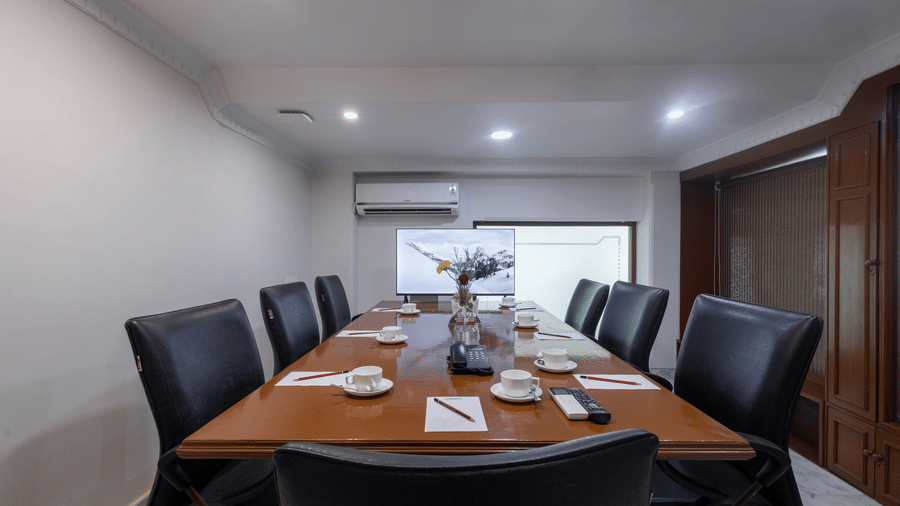 A private meeting room with a large wooden table, set for a meeting with black leather high-backed chairs at Pravasa Stay, Vadodara.