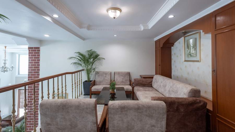 Cosy mezzanine lounge area with comfortable sofas, low tables, and wooden accents, brightly lit at Pravasa Stay, Vadodara.