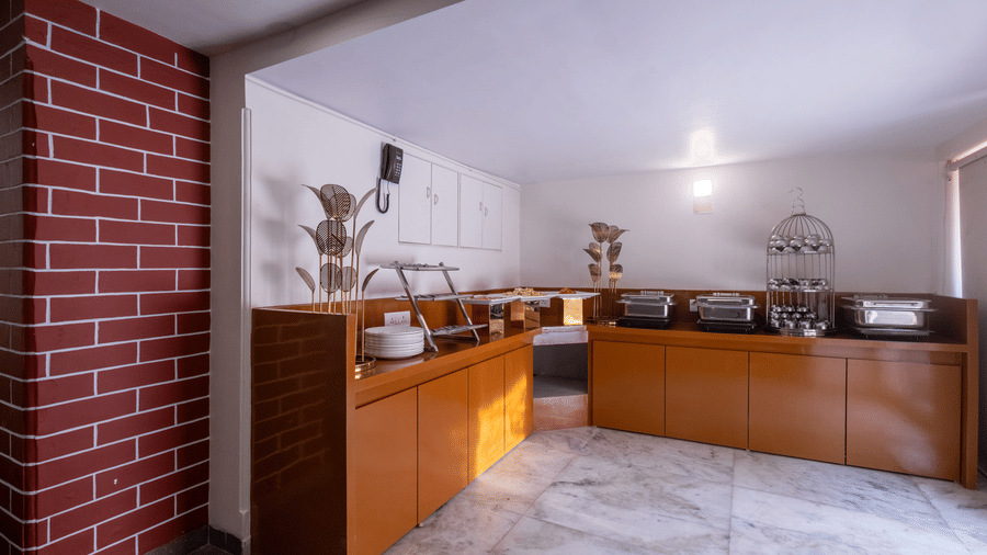 A breakfast or buffet serving area with wooden counters, a red brick feature wall, and marble flooring at Pravasa Stay, Vadodara.