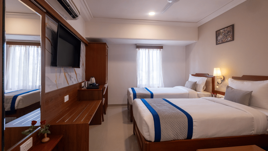 View of the twin-bedded hotel room, reflected partially in the large, dark wooden mirror over the desk/console at Pravasa Stay, Vadodara.