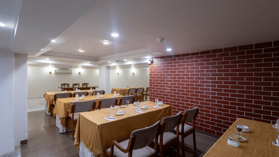 Dining space configured with long tables and chairs, covered in orange cloth, suitable for a meeting or group event at Pravasa Stay, Vadodara.