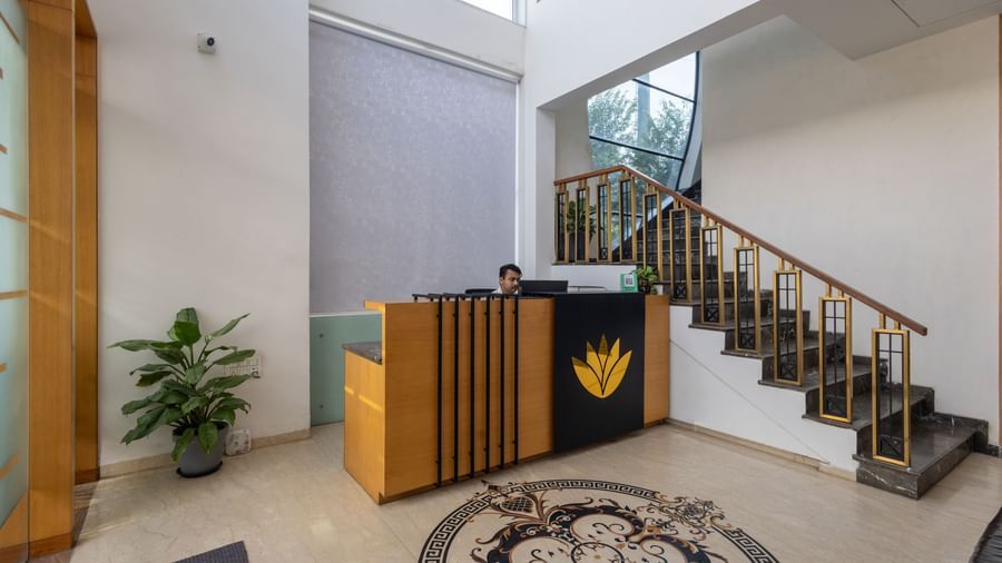 Lobby and reception desk of Pravasa Stay Vijay Nagar, Indore, showcasing a desk, a flight of stairs leading to the floor above, and a floor with patterned tiles in the centre.