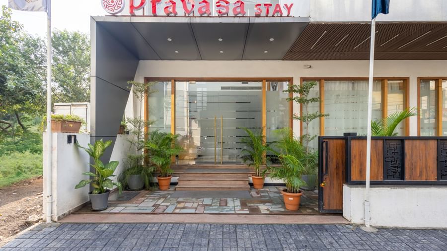 Facade and entry to Pravasa Stay Vijay Nagar, Indore, lined by potted plants on both sides, and an illuminated logo placed on the elevated ceiling.