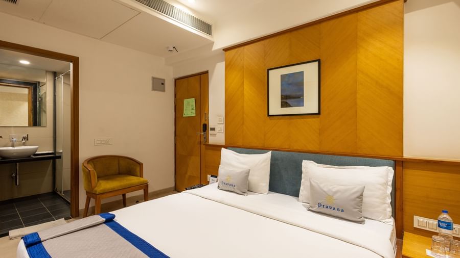 Queen size bed, seating chair, and a door opening to the bathroom seen in a Premium Room of Pravasa Stay Vijay Nagar, Indore.