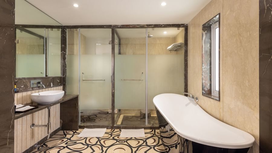Bathroom of Suite at Pravasa Stay Vijay Nagar, Indore, seen with separated shower area and toiler, a bathtub placed outside opposite the vanity area.