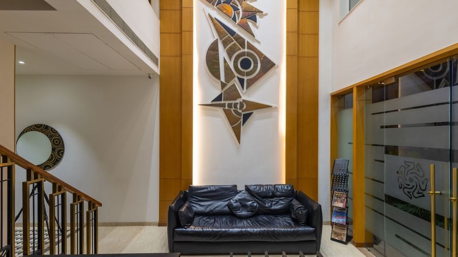 Lobby area of Pravasa Stay Vijay Nagar, Indore, featuring a multi-seater sofa facing the reception desk, with a patterned highlighted wall behind.