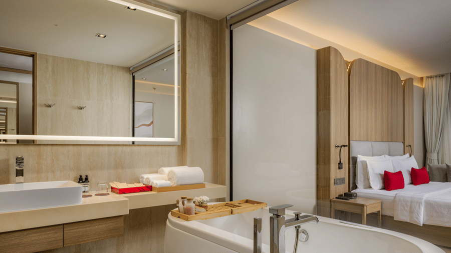 A bathroom of Deluxe Jet Tub room featuring a bathtub, vanity counter, and a mirror with an adjoining room visible at Ramada Palace.