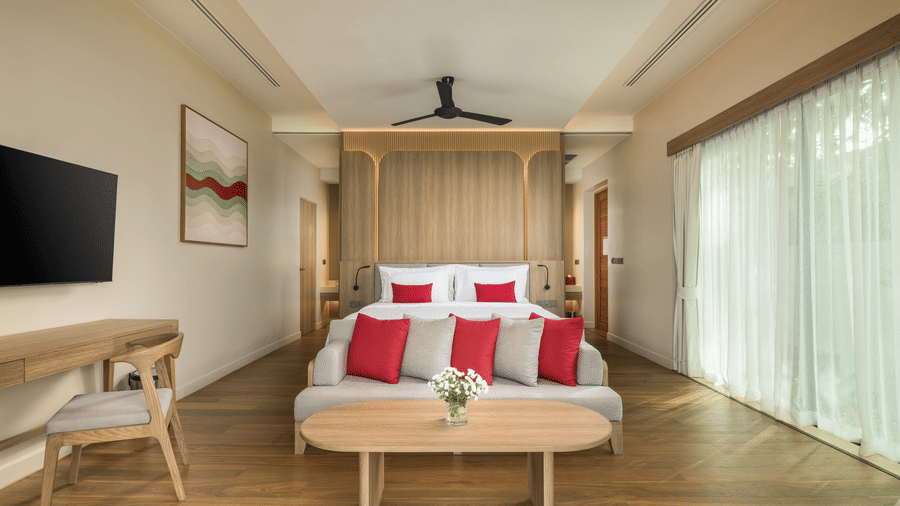 A bedroom of Oceanfront Villa with a large bed, central seating table, bedside furniture, and floor-to-ceiling curtains at Ramada Resort.