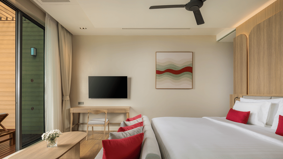 A bedroom of Oceanfront Villa with a large bed, bedside seating, a wall-mounted television, and balcony access at Ramada Resort.