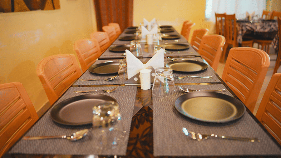 A long, elegantly set restaurant dining table with orange chairs and formal place settings for a group.