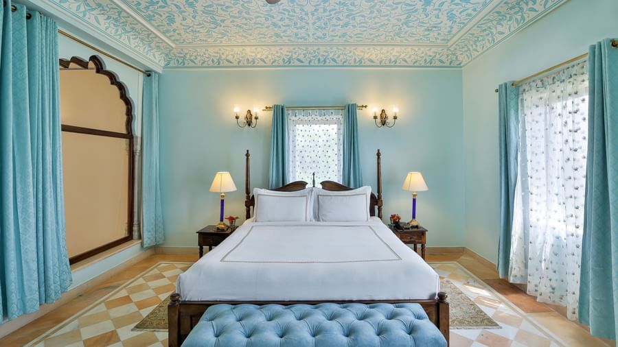 A bedroom at Royal Heritage Haveli with light blue walls, a bed with a white spread, and one arched window
