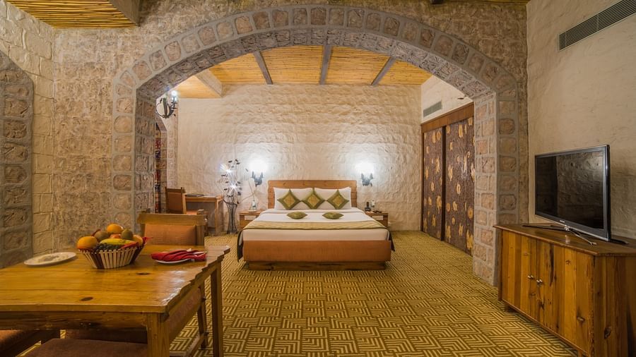 A spacious hotel bedroom with stone walls, wooden furniture, and a welcoming bed under a vaulted ceiling at  Sitara Luxury Hotel in Hyderabad near Ramoji Film City.