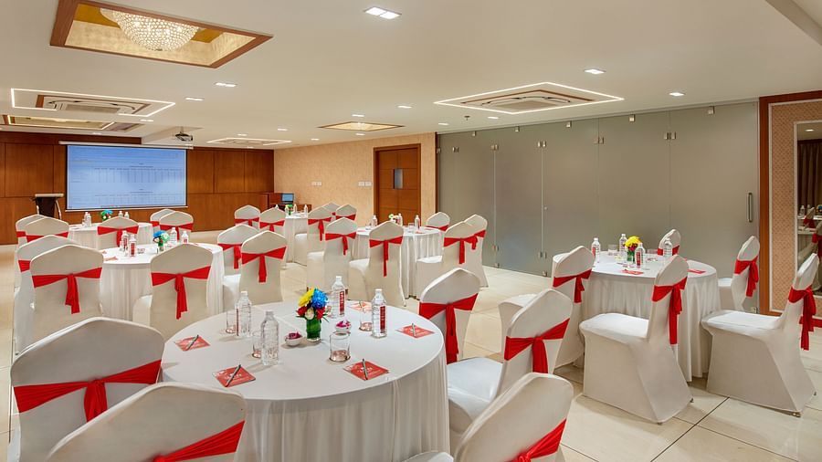 A brightly lit banquet hall set up with round tables and decorated chairs, ready for an event - SK Lords Inn Ahmedabad
