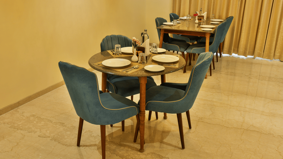 An intimate dining setup featuring a circular wooden table with blue velvet chairs and formal place settings - Tathastu Chavri Resort, Jawai