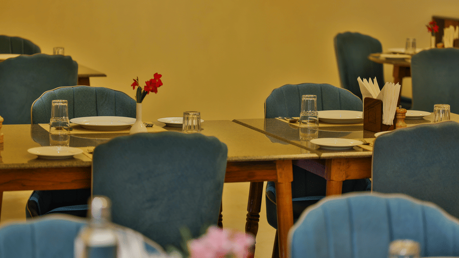 A detailed view of wooden dining tables paired with plush teal chairs and formal glassware - Tathastu Chavri Resort, Jawai