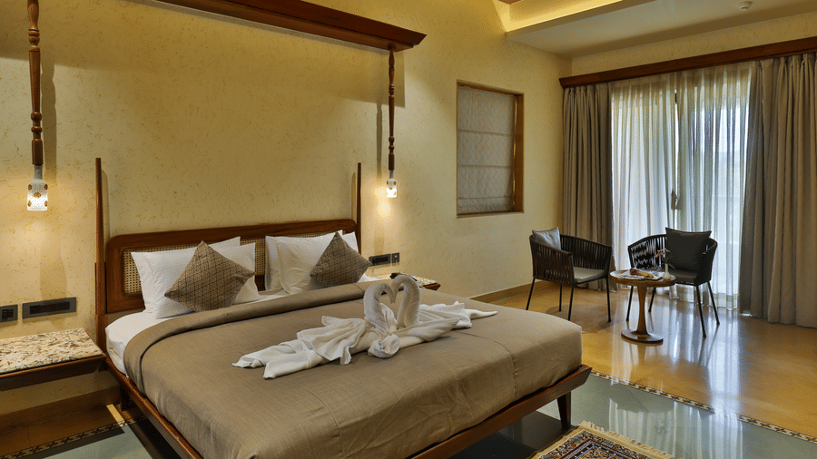 A modern bedroom setup showing a large bed, side tables, and glass doors leading to a balcony - Tathastu Chavri Resort, Jawai