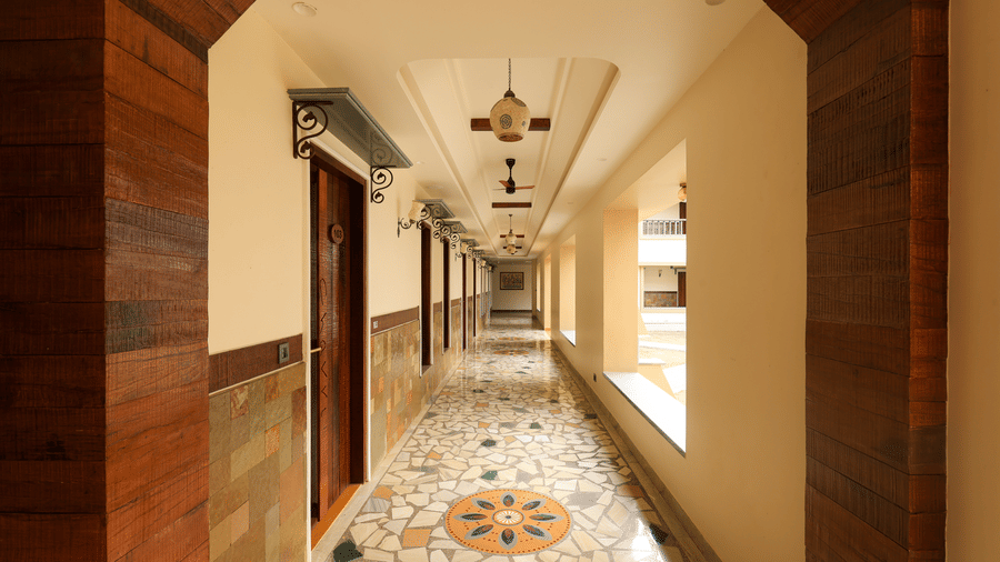 A long, brightly lit resort hallway featuring decorative floor tiling, warm wood panelling, and elegant ceiling fixtures - Tathastu Chavri Resort, Jawai