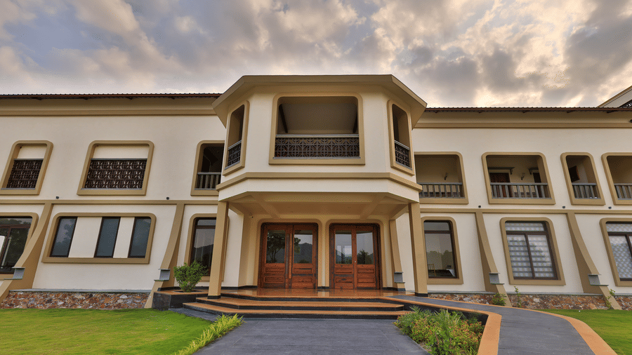 A ground-level view of the resort's main building facade with wooden doors and an arched balcony under a cloudy sky - Tathastu Chavri Resort, Jawai