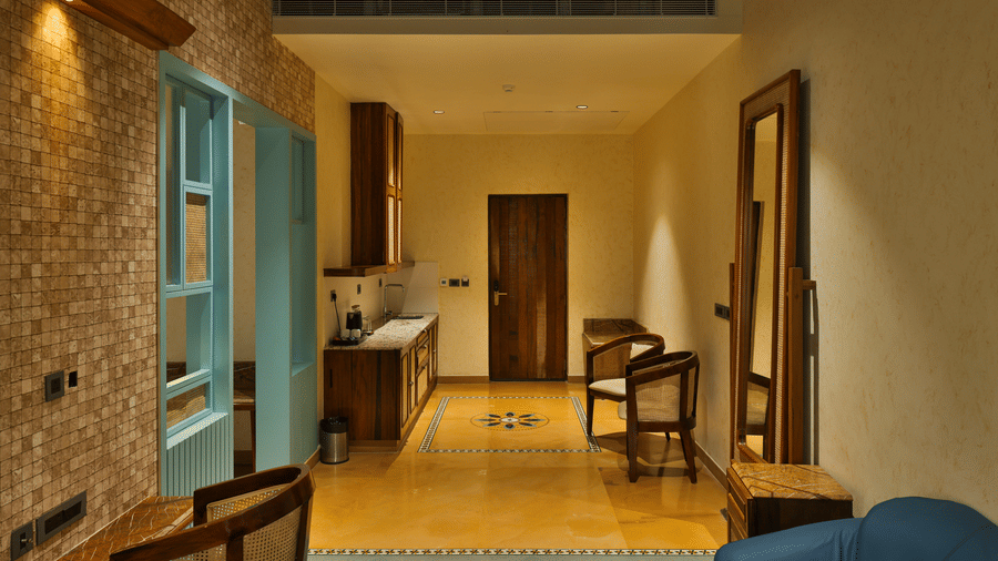 An interior view of a suite entrance featuring warm lighting, stone-textured walls, and a large mirror - Tathastu Chavri Resort, Jawai