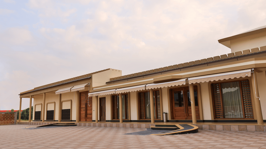 A wide view of the resort's exterior showcasing a large paved courtyard and the main building with outdoor awnings - Tathastu Chavri Resort, Jawai
