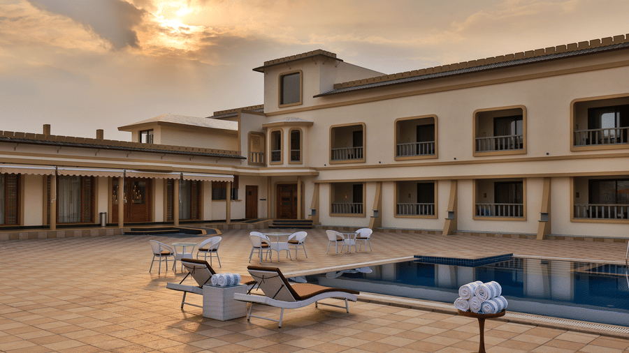 An outdoor swimming pool and patio area with lounge chairs under a soft sunset sky - Tathastu Chavri Resort, Jawai