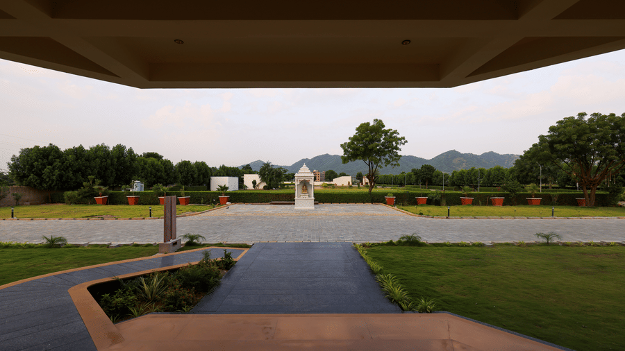 A view from under a covered entryway looking out toward a paved pathway, green lawns, and distant hills - Tathastu Chavri Resort, Jawai