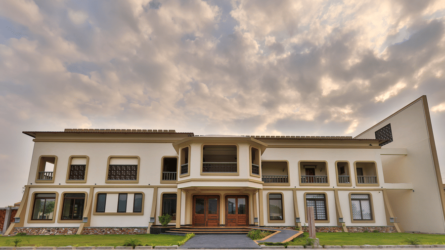 A wide shot of the main resort building featuring multi-level balconies and large windows under a dramatic sunset sky - Tathastu Chavri Resort, Jawai