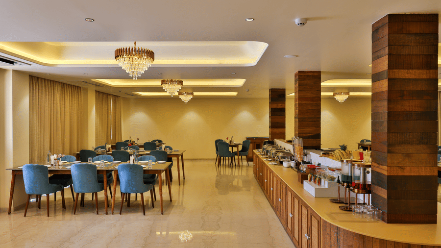 A wide interior shot of the dining area showing the long wooden buffet counter and elegant chandeliers - Tathastu Chavri Resort, Jawai