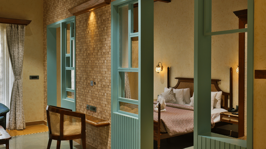 A view looking through a decorative teal wooden partition into a cosy, well-appointed bedroom - Tathastu Chavri Resort, Jawai