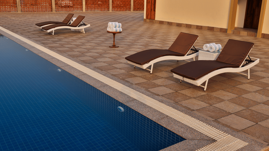 A close-up of the outdoor swimming pool featuring white and brown reclining lounge chairs on the patio - Tathastu Chavri Resort, Jawai