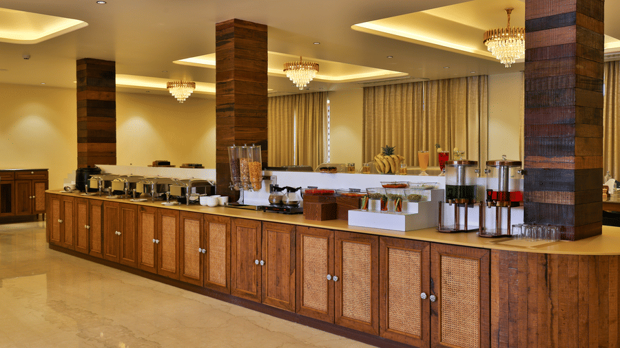 A long, elegant wooden buffet counter in a brightly lit dining hall with modern pillars - Tathastu Chavri Resort, Jawai