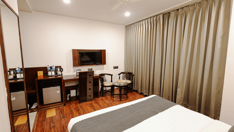 Executive Room at TGI Apple Inn, Ajmer Road, Jaipur featuring a bed, desk, television, chairs, fridge, mirror, and curtains.