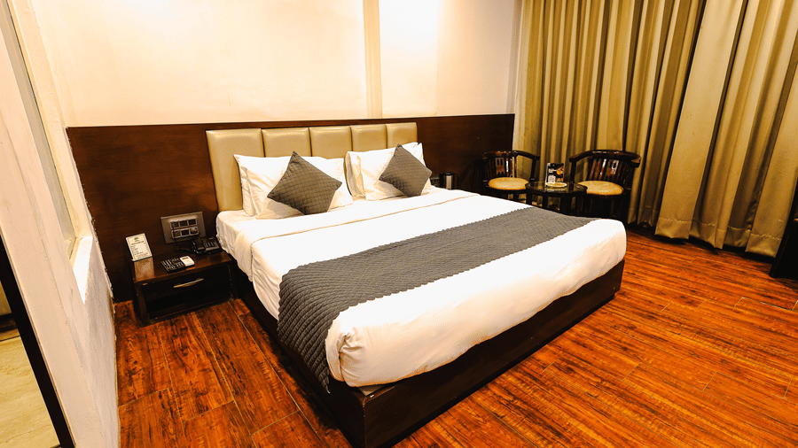 Bright guest room with plush king bed, warm interiors and floor-to-ceiling curtains at TGI Apple Inn, Ajmer Road, Jaipur.