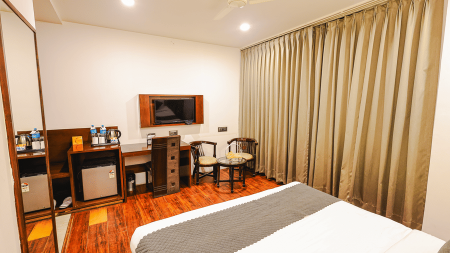 Royal Executive Room at TGI Apple Inn, Ajmer Road, Jaipur featuring a bed, desk, television, chairs, fridge, mirror, and curtains.