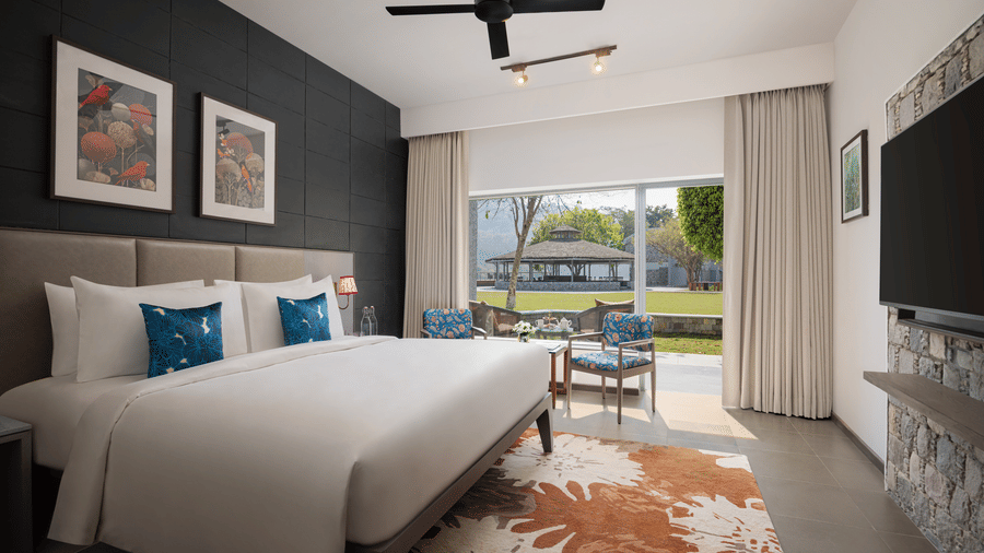 Spacious bedroom with king size bed, wall art, ceiling fan, and large window overlooking greenery at The Corbett Hideaway.