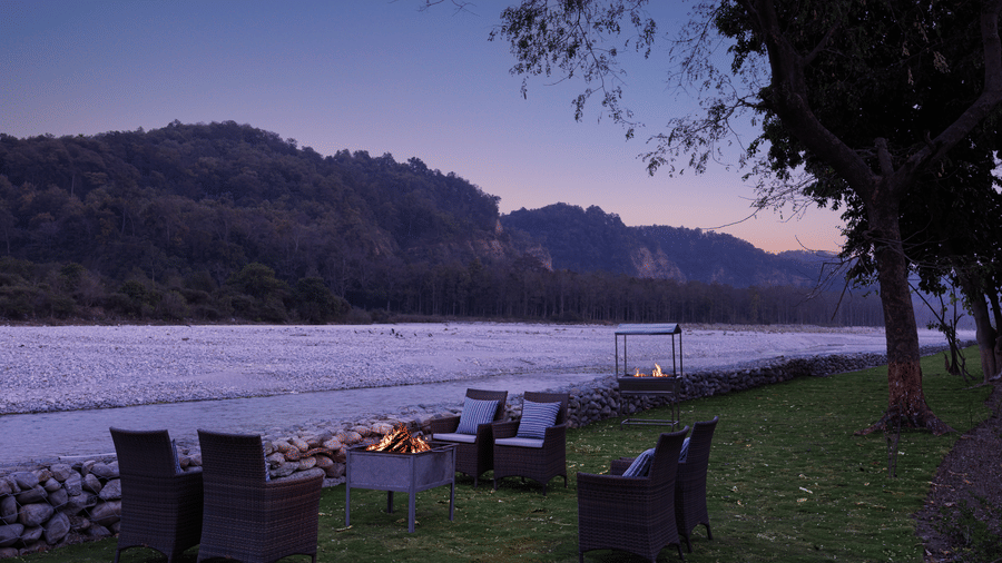 Riverside outdoor dining setup with tables and chairs overlooking scenic hills at The Corbett Hideaway.