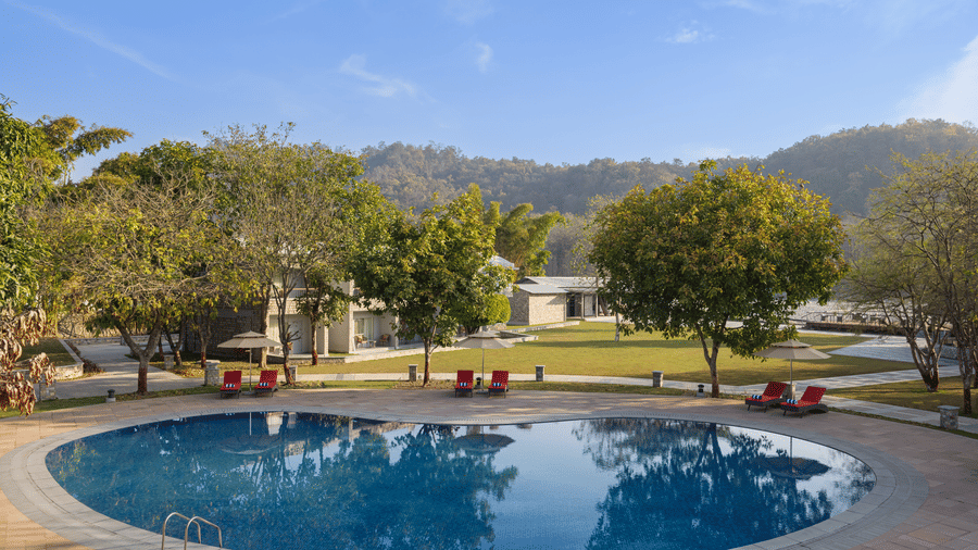 Outdoor swimming pool surrounded by lush greenery and hills under clear sky at The Corbett Hideaway.