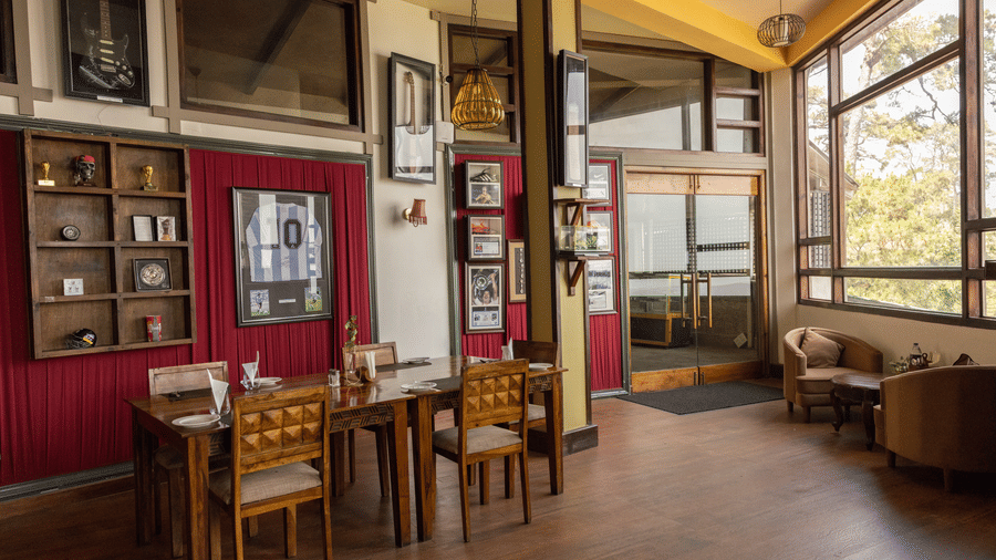 A dining space with several wooden tables, several wall arts, and chairs. | The Heritage Club, Tripura, Castle, Shillong