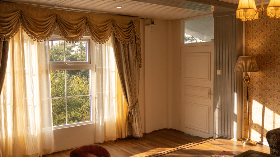 A room at The Heritage Club, Tripura, Castle, Shillong, featuring a large window covered with curtains and lamps.