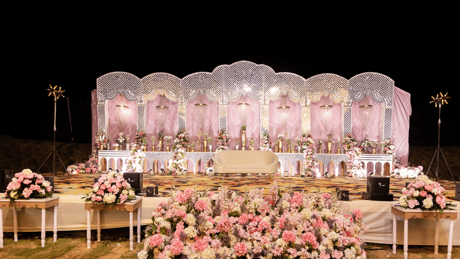 An outdoor wedding setup is shown at night, featuring a stage, seating, and floral arrangements |The Qualia Resort Club & Brewery, Udaipur