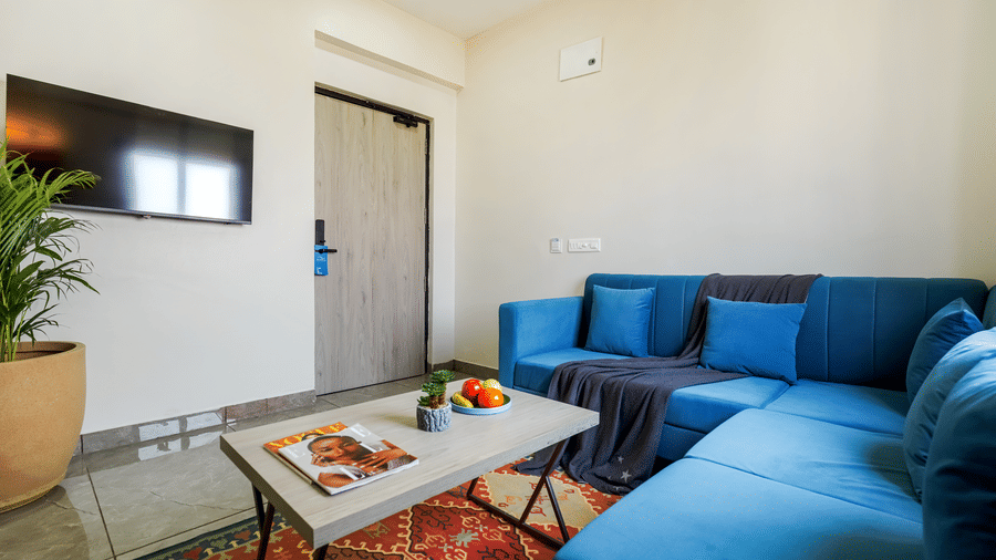 A living room area of a room at Urban Suites by BluSalzz, Jaipur, with a blue sofa, a coffee table on a patterned rug, and a door leading outside.