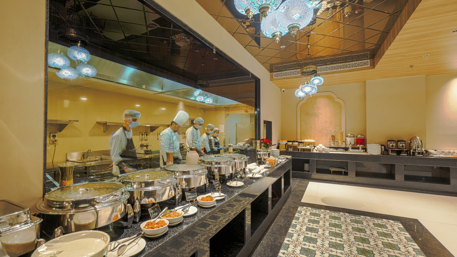 The well-lit Urban Rasoi at Urban Suites by BluSalzz, Jaipur, featuring buffet station with various culinary artists serving food items in serving dishes.