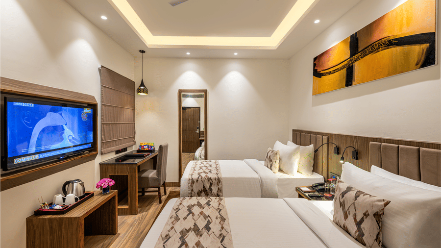 Modern designed elegant room with two twin beds, a flat-screen TV, a work desk and colourful abstract wall art at Lords Eco Inn Dehradun.