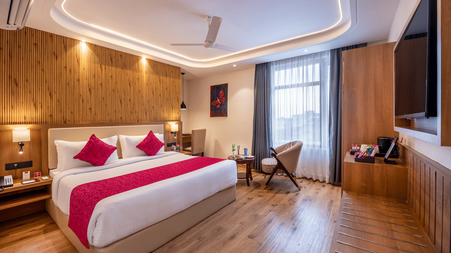A spacious bedroom at Lords Inn Katra with a king size bed, an armchair, a wall mounted television, panelled walls, and side tables.
