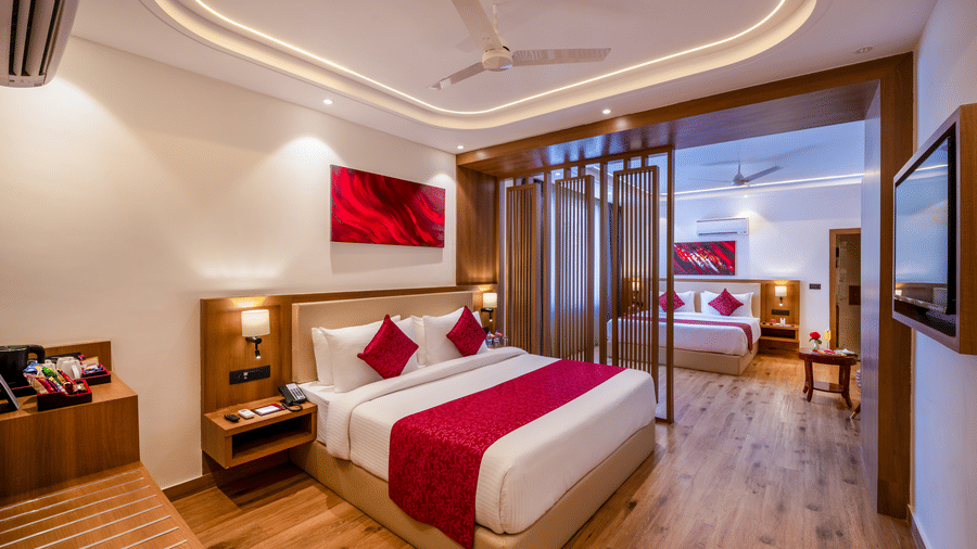 An interconnected suite at Lords Inn Katra showing a king size bed, a wooden partition screen, a television, and another room beyond.
