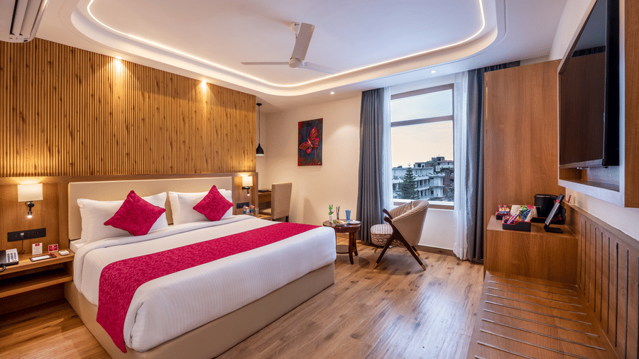 A spacious hotel room at Lords Inn Katra featuring a wide king size bed, a polished wooden wall panel, and a large window overlooking the hills.