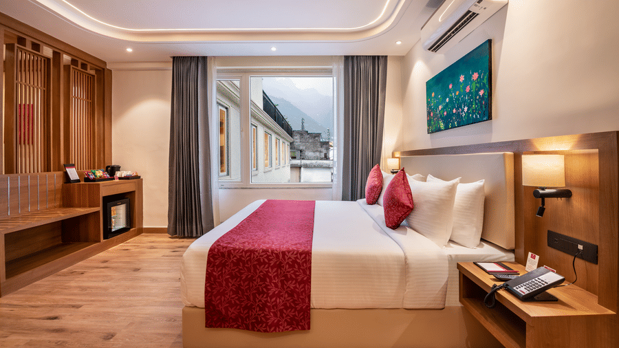 A hotel bedroom at Lords Inn Katra featuring a king size bed, a side table with a telephone, and a glass window showing adjacent structures.