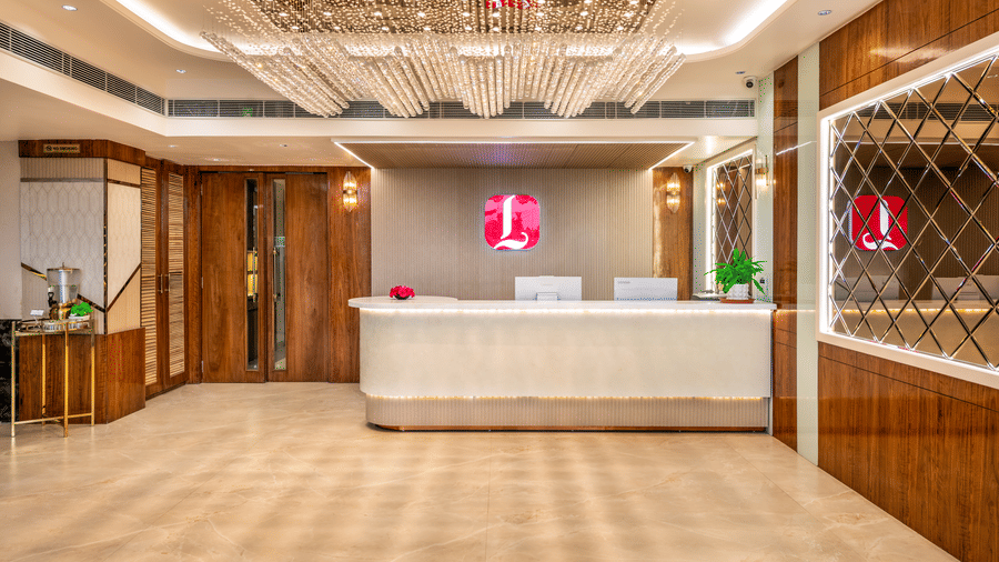 Front desk reception area at Lords Inn Sangam, Bhopal showcasing a sleek white counter, warm wood paneling, and elegant patterned ceiling design.