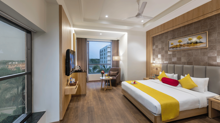 A premium room in Lords Inn Somnath with modern interiors, featuring a neatly made double bed and a large window offering a view of the outdoors.